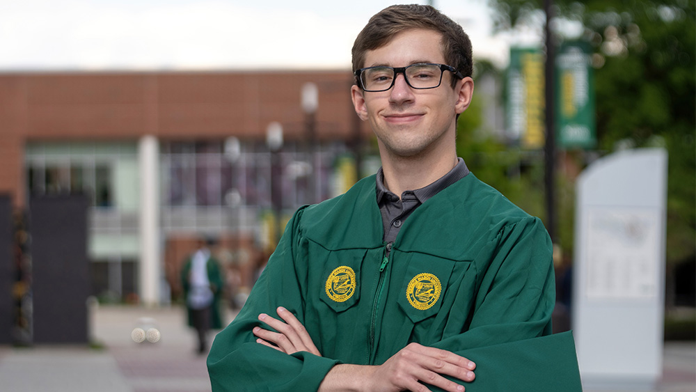 Graduate brad byrne is part of a long family legacy. Brad is wearing GMU colors green gown with gold patches. He holds a green cap.