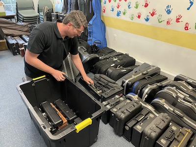 A man is packing smaller instrument cases into a larger bin, to more easily transport the cases.