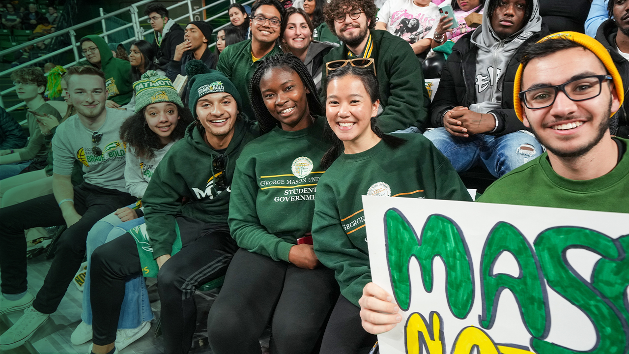 A group of Mason students smile together in the stands at a Homecoming game.