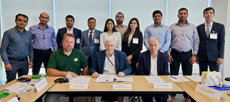 A group of people pose for the camera from behind a table in a conference room.