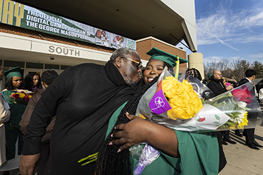 A graduate holding flowers gets a kiss on the cheek from her father.