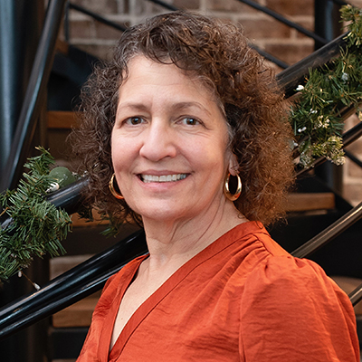 A woman wearing an orange shirt stands outside while smiling