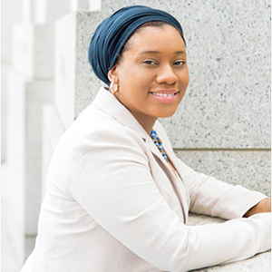 A woman in a white jacket stands outside and smiles