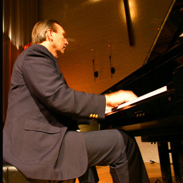 Wade Beach playing piano in a dark suit