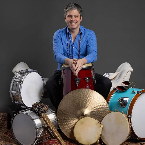 Juan Megna sitting with his percussion set in a blue button up
