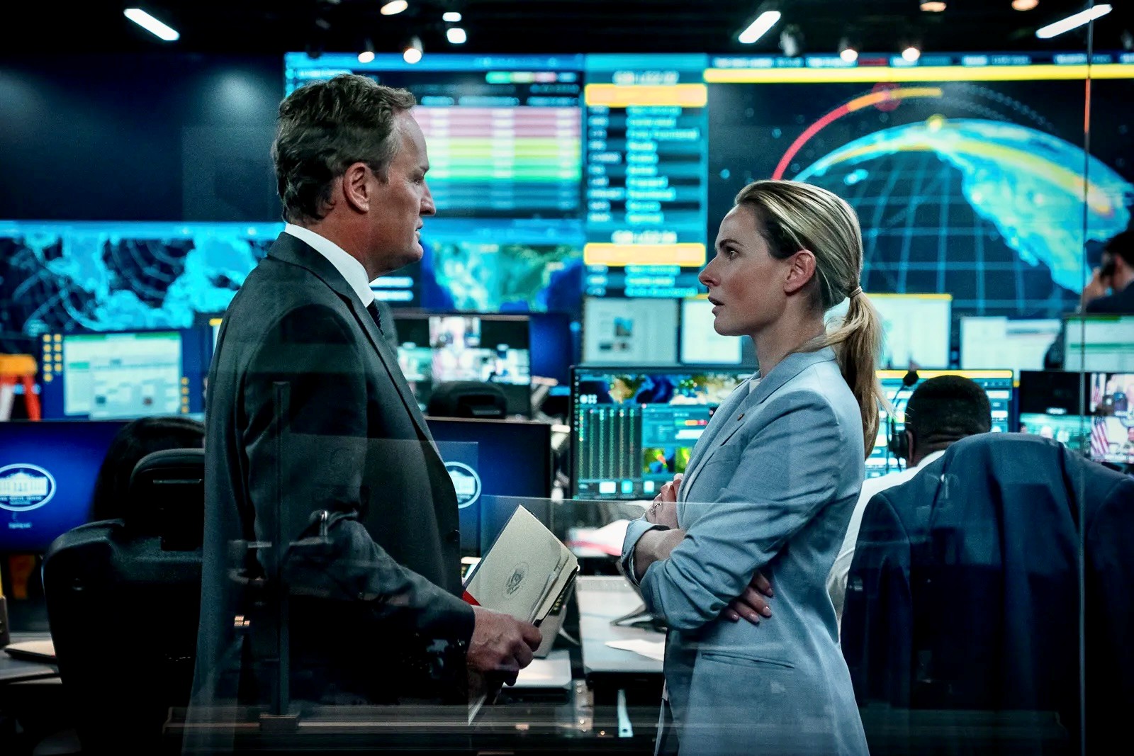 A man in a dark suit faces a woman in a blue outfit.