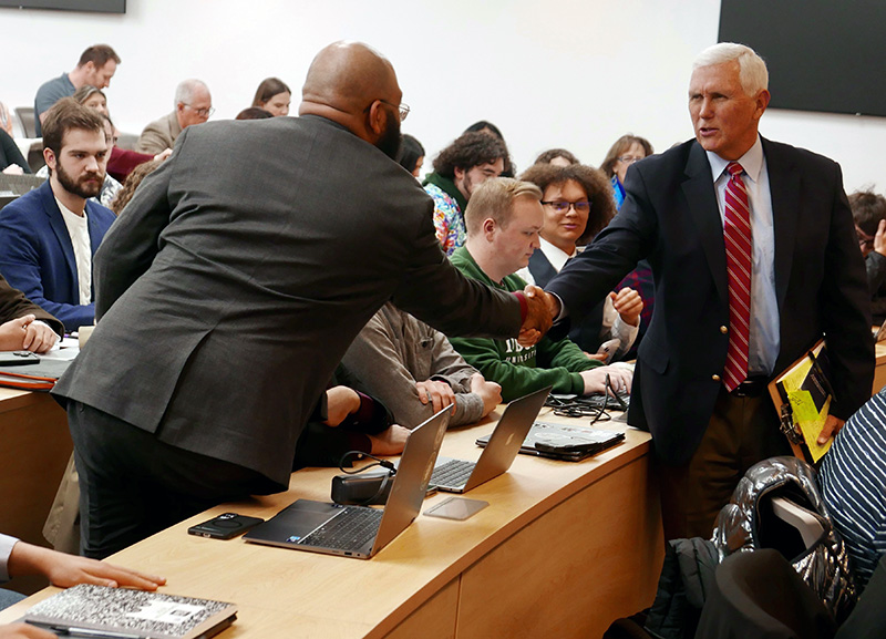 A bald man reaches to shake hands with a man with white hair.