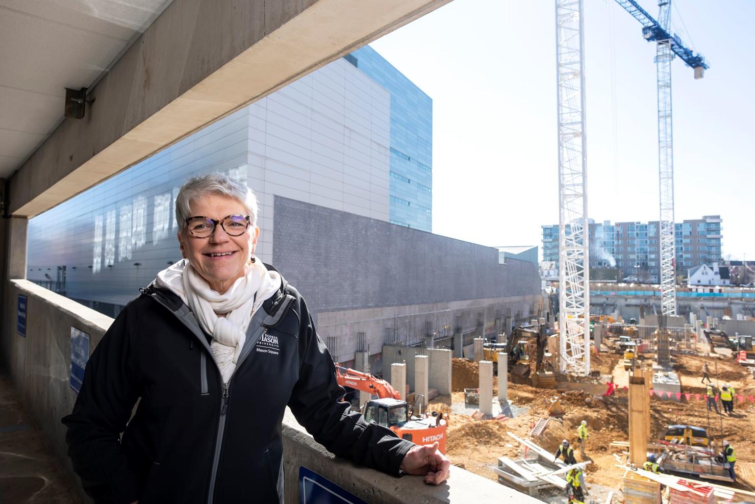 Woman stands inside a parking garage overlooking the construction site of Fuse at Mason Square. Cranes line the sky with other tall buildings in the background