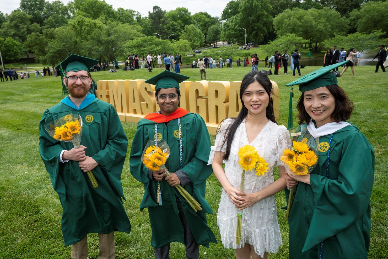 Graduates gather together holding bouquets near Mason Pond