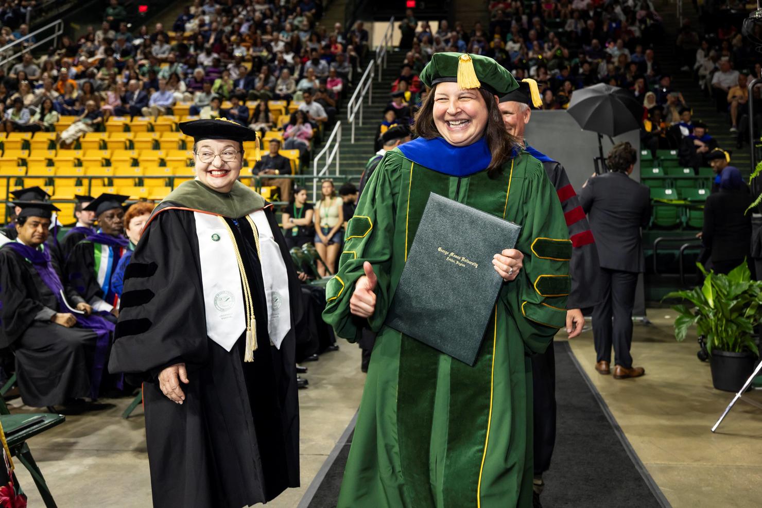 Graduate proudly walks across stage with her diploma while giving a thumbs up