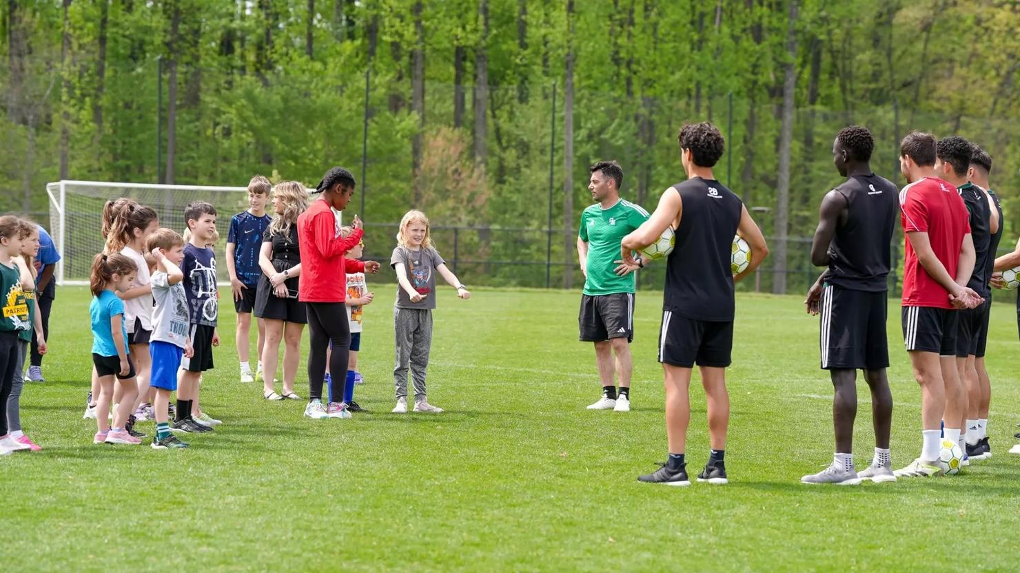Children and members of the George Mason men's soccer team stand together on the soccer field during a clinic