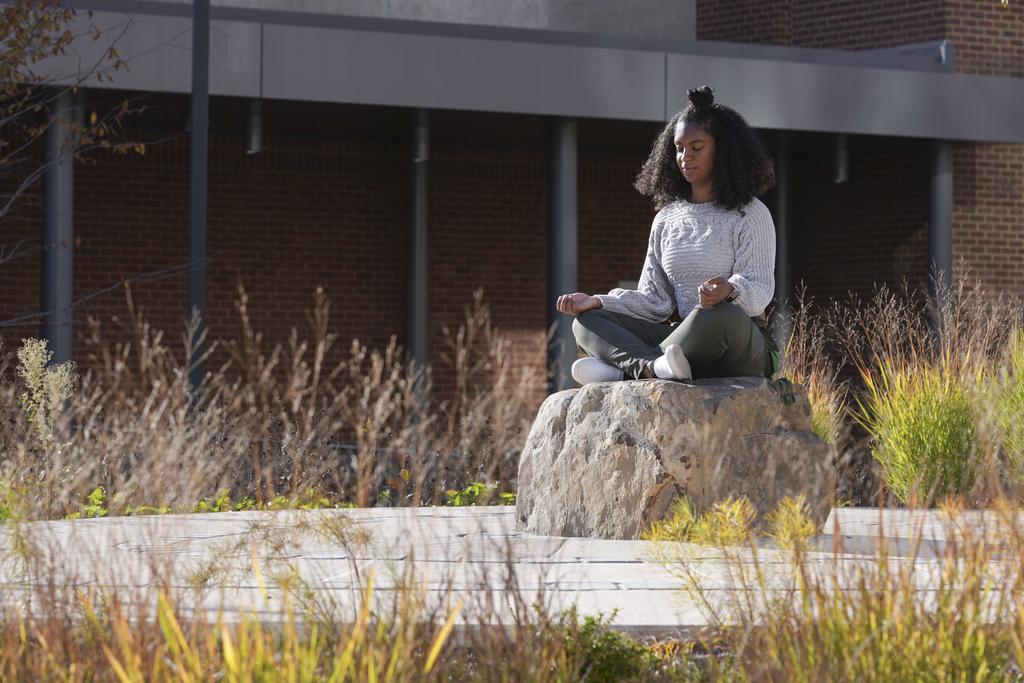 Student sitting on a rock meditating.