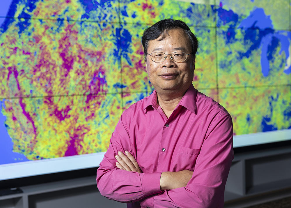 Dr. Liping Di stands in front of a large electronic map