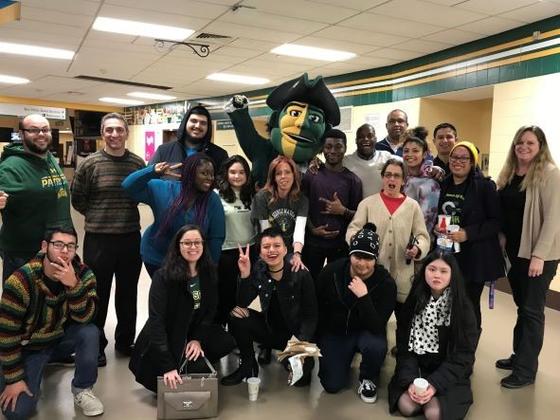 A group of high school students pose for a photo with Mason employees on the concourse at EagleBank Arena. The Patriot mascot stands in the center.