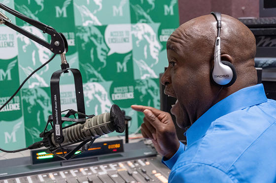 University President Gregory Washington sits in front of a microphone talking. 