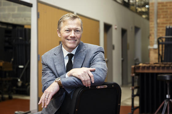 Matthew Desmond sits backwards in a chair, grinning for the camera in his suit and tie.
