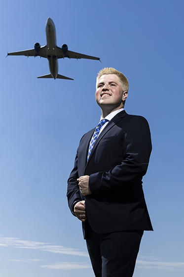 Mack Freilich poses below a flying airplane against a blue sky