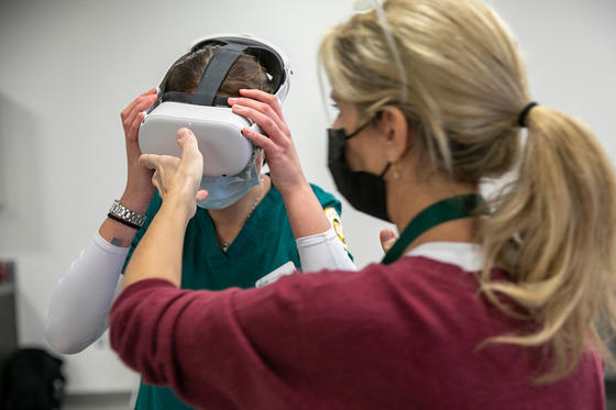 A woman helps a nursing student adjust a VR headset on her head.