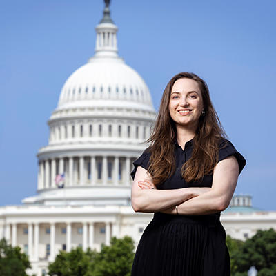 A woman in a dark top stands in front of the Capitol building.