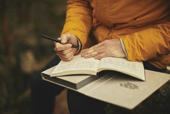 Person in yellow shirt holding a journal open with a pen.