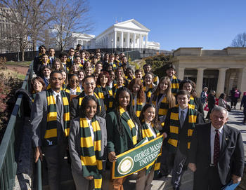 Mason students dressed with green and gold scarves pose in front of the VA state capitol.