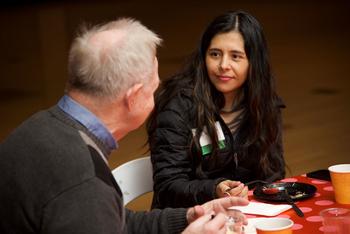 A woman sits at a table and listens to the man speaking next to her. The table is set for breakfast.