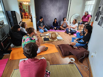 Students sit on floor with colorful yoga mats, circled around a centerpiece of books and a hat.