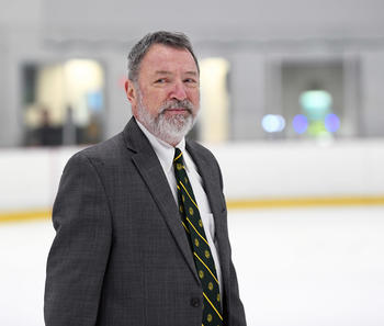 Former George Mason Ice Hockey coach Steve Hyjek poses standing on a hockey rink.