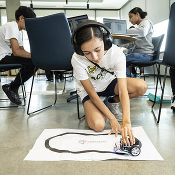 A student wearing headphones places the micro:bit robot on a paper track