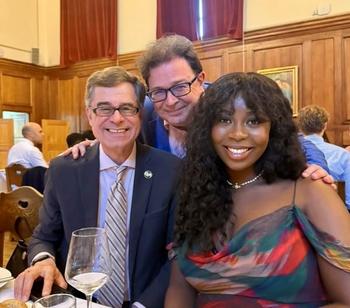 Two men wearing glasses and a woman smile for a photo while eating dinner